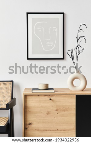 Stylish interior of living room with mock up poster frame, wooden commode, book, leaf in ceramic vase and elegant personal accessories. Minimalist concept of home decor. Template.