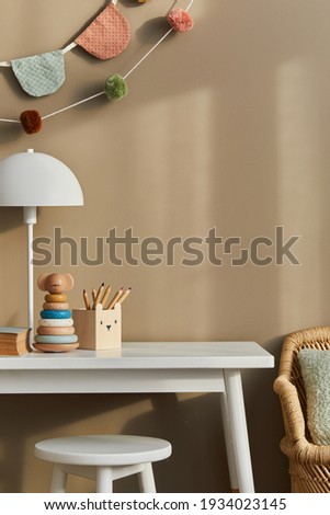 Interior design of stylish kid room space with white shelf, wooden toys, child accessories, white lamp, cozy decoration and hanging cotton flags on the beige wall. Template.