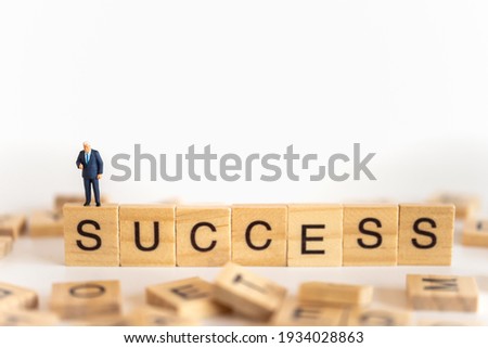 Business and work concept. Businessman miniature figure people standing with show thumb up on wooden letter block wording Success.