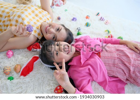 The young mother and her daughter lay down together on the carpet to playing easter eggs. 