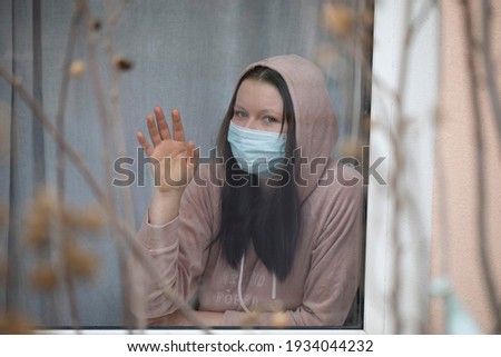 Coronavirus . Sick girl looking through the window and wearing medicine mask . Quarantine . Pandemic . Patient isolated to prevent infection of pandemic , epidemic Covid-19