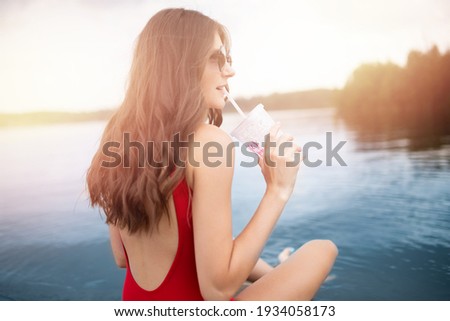 Young woman relax in red swimsuit holds glass with cocktail on beach on glasses, sunlight.