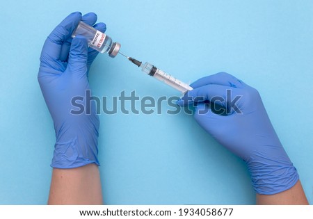 Doctor's hand in blue medical gloves holding a plastic syringe with vaccine on blue background. 
