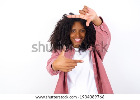 young beautiful African American woman wearing pink jacket against white wall making finger frame with hands. Creativity and photography concept.