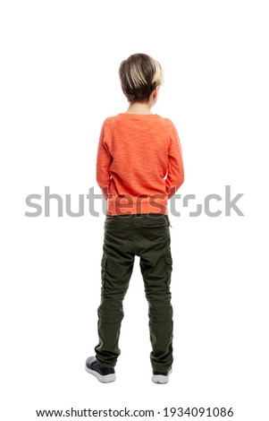 A 9-year-old boy stands in jeans and an orange sweater. Full height. Isolated on a white background. Vertical. Back view. Royalty-Free Stock Photo #1934091086