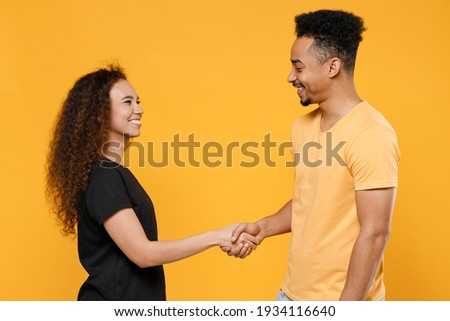 Young couple two friends together family smiling african man woman in black t-shirt hold hands folded handshake gesture friendship business greet concept isolated on yellow background studio portrait Royalty-Free Stock Photo #1934116640