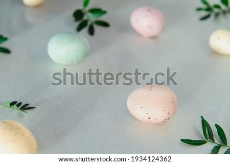 Easter holiday concept. Pastel colors painted eggs with small fresh green leaves on white background. Soft natural light. Festive spring mood. Easter natural decor. Soft selective focus. Copy space