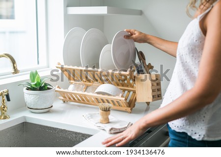 Woman washing dishes in kitchen using eco friendly brush and drying rack Royalty-Free Stock Photo #1934136476