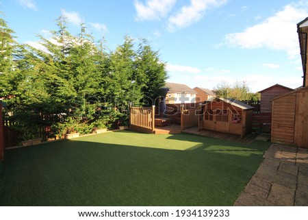 garden with astroturf lawn with wooden deckig area, childrens play house, hut, flowers and trees. Royalty-Free Stock Photo #1934139233