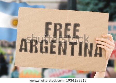 The phrase " Free Argentina " on a banner in men's hand with blurred Argentinian flag on the background. Protest. Riot. Violence. Economic crisis. Collapse. Politics. Streets. Save. Cruelty