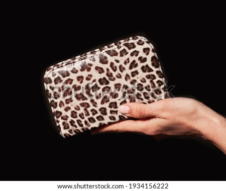 woman's hand holding an animal print wallet on a black background