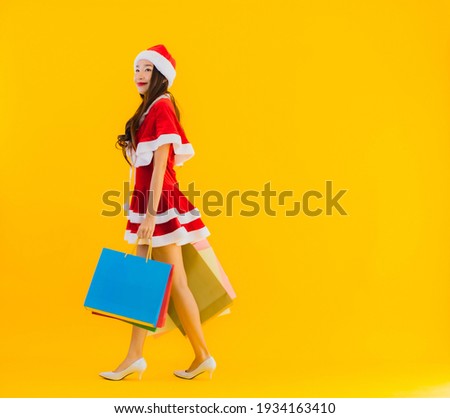 Portrait beautiful young asian woman wear christmas clothes hat with a lot of shopping bag on yellow isolated background