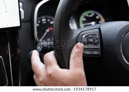 Unrecognizable man driver activating the adaptive cruise control or steering assistant on the control stick behind steering wheel  in electric vehicle - EV. Driving Assist system in modern car. Royalty-Free Stock Photo #1934178917