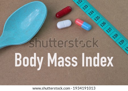 Pill capsules, measuring tape and spoon over brown background written with BODY MASS INDEX.
