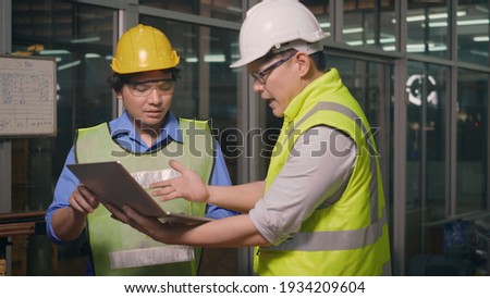 Two factory industrial workers technician or engineer and manager wear uniforms safety feeling upset with the engine machine of the factory arguing about planning procedure of work on laptop computer Royalty-Free Stock Photo #1934209604