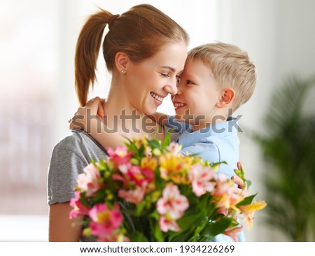 Optimistic family: mother with bouquet of  alstroemeria laughing and touching nose with happy son  during holiday celebration  mothers day at home Royalty-Free Stock Photo #1934226269
