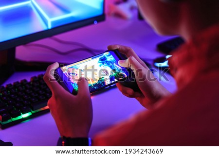 Gamer playing online game on smart phone in dark room. e-Sport Games compilation and Internet Championship. Royalty-Free Stock Photo #1934243669