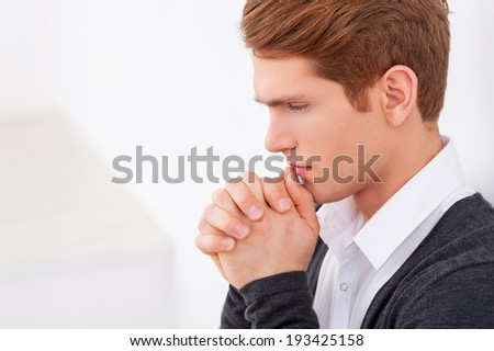 Worried about business. Side view of thoughtful young man holding hands clasped near mouth and looking down while standing isolated on white