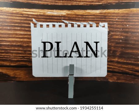 Blur wooden clothespin with blur sheet of paper.Text PLAN on white background.Business concept. 