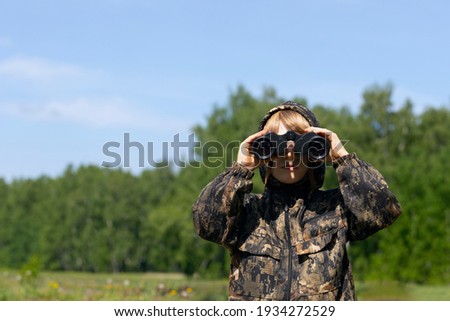 Caucasian boy in masking camouflage uniform with binoculars. Plays scout, military or hunter.