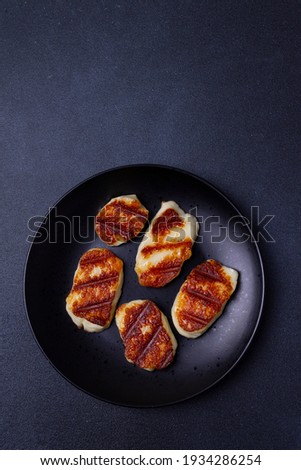 Toasted Halloumi cheese on a black plate on a black background. Vertical orientation. Copy space.