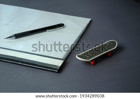 Skateboard finger, folder for papers and pencil on gray table. Mini skate next to the binder folder. Side view, selective focus.