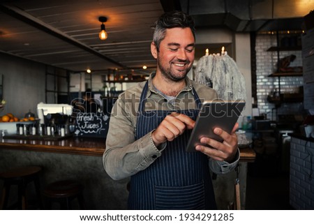 Male waiter smiling while receiving monthly salary on digital tablet in trendy cafe  Royalty-Free Stock Photo #1934291285