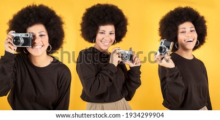 Young beautiful African American mixed race taking photo with retro camera on yellow background, copy space