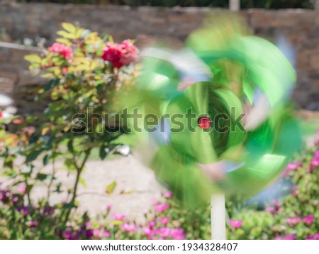 Greenish toy pinwheel creating a colorful trail from the movement caused by the wind in the center of a garden with colorful flowers in the background