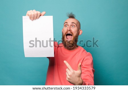 Bearded european man in casual peach isolated on turquoise background holding white empty paper board point index finger