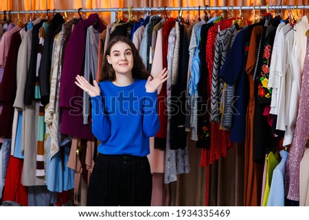 handsome teenager with her hands up, looking at the camera. Beautiful young woman near rack near hangers with clothing. shopping, fashion, style and people concept