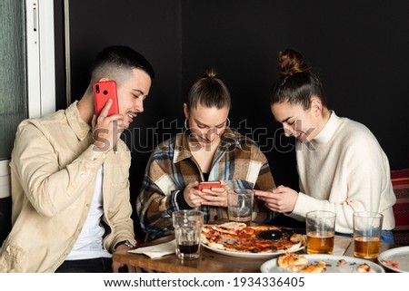 three young people are answering their respective mobile phones during a dinner.