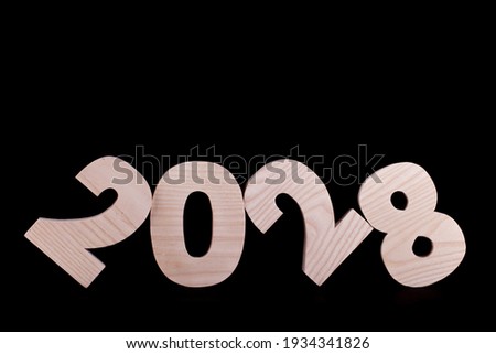 2028 year large wooden numbers tilted and leaning. Hardwood characters on a black background