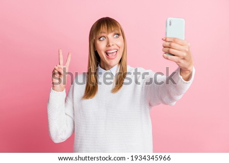 Photo of young happy positive smiling good mood woman take selfie on phone show v-sign isolated on pink color background