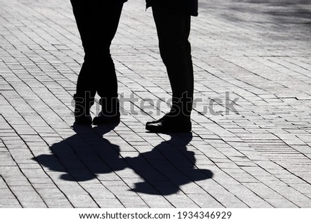 Silhouettes and shadows of couple on the street, two people standing on pedestrian sidewalk. Concept of relationships, city life, dramatic stories