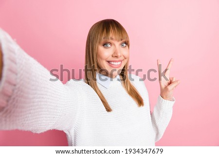 Portrait of young lovely pretty smiling good mood cheerful woman take selfie showing v-sign isolated on pink color background