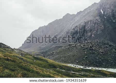 Atmospheric alpine landscape with narrow valley with mountain creek and sharp rocks under gray sky. Bleak highlands scenery with pointed rockies on mountainside and mountain creek in overcast weather. Royalty-Free Stock Photo #1934351639