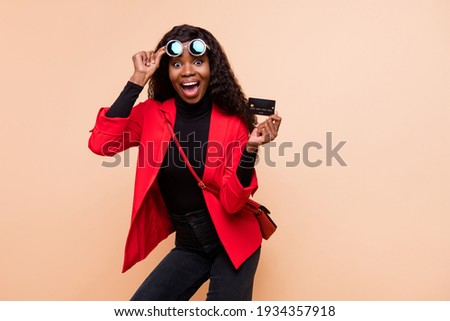 Photo of shocked brown haired afro american woman wear glasses hold debit card isolated on beige color background