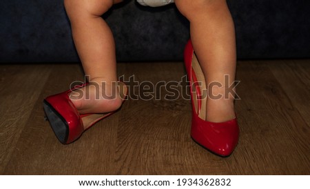 Pretends to be an adult. Close-up shot of boy's feet in oversized red high-heeled shoes with copy space.