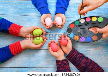 Mom helps children paint holiday eggs with colored paints and a brush for Easter.