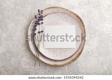 White paper invitation card, mockup with lavender on ceramic plate and gray concrete background. Blank, flat lay, top view, still life, copy space.