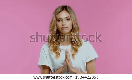 young woman with praying hands looking at camera isolated on pink