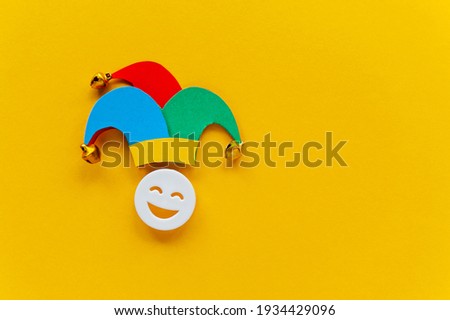 Jester hat with laughing face over yellow background. First April card with emoji. Copy space for text, top view.  