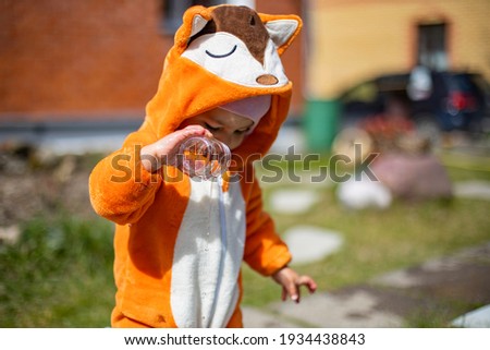 adorable little toddler playing with water in the backyard in sunshine. child in a fox costume 