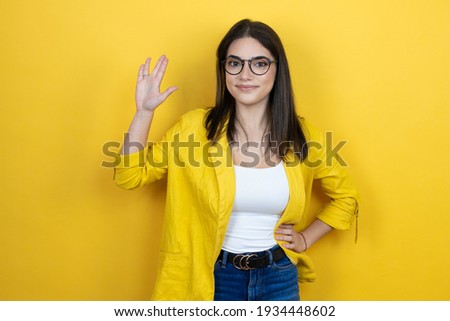 Young brunette businesswoman wearing yellow blazer over yellow background doing hand symbol