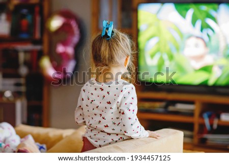 Cute little toddler girl in nightwear pajamas watching cartoons or movie on tv. Happy healthy baby child at home