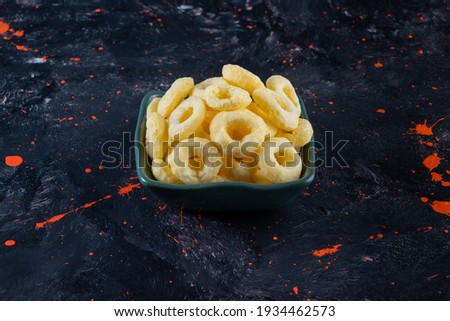 On navy blue table with orange spots, corn rings in bowl. High quality photo