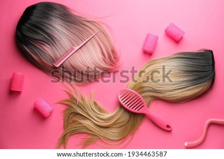 Female wigs, brush, comb and curlers on color background Royalty-Free Stock Photo #1934463587