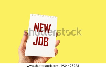 Hand holds notepad on yellow background with text NEW JOB