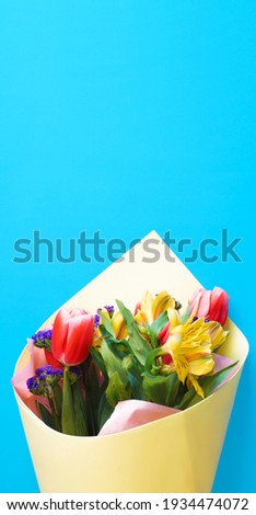 Decorated bouquet of flowers on a blue background, close-up. Lilies and tulips. Vertical photo with copy space.